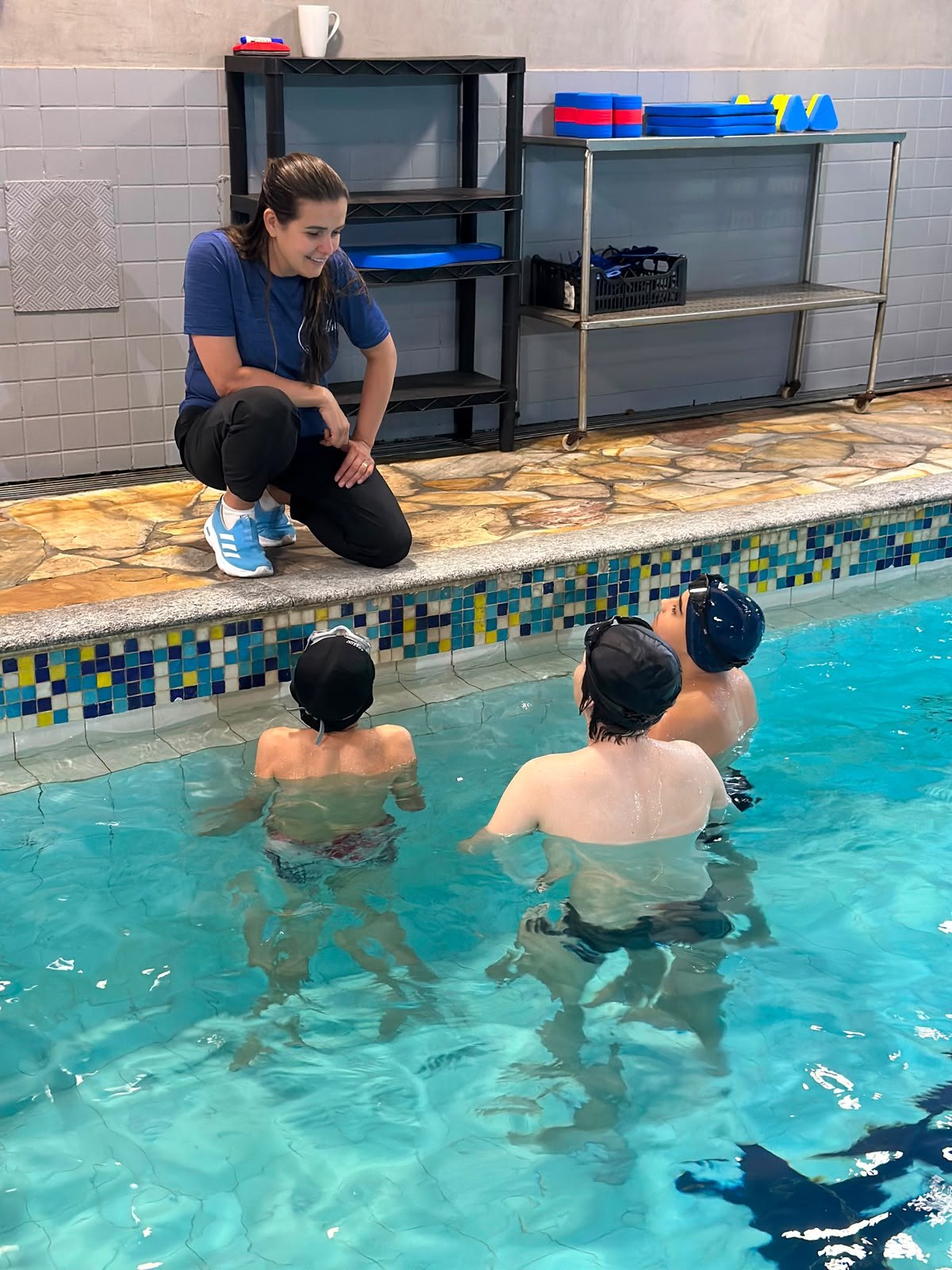Professora acompanhando alunos na piscina da Academia Mergulho